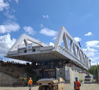 A grey steel box girder bridge span hangs over the road