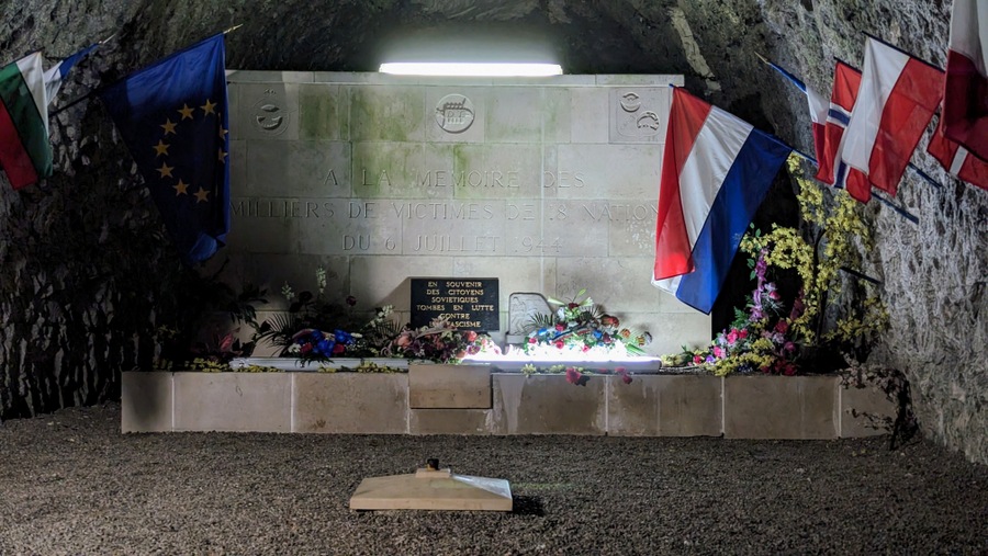 A large memorial headstone fills the end of a short tunnel, with national flags on the walls