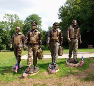 Four life-size bronze statues of USAAF airmen striding towards the camera on a grassy hill