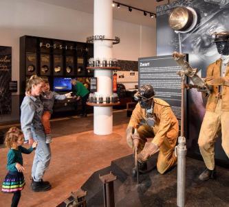 Visitors look at two miner mannequins in orange overalls