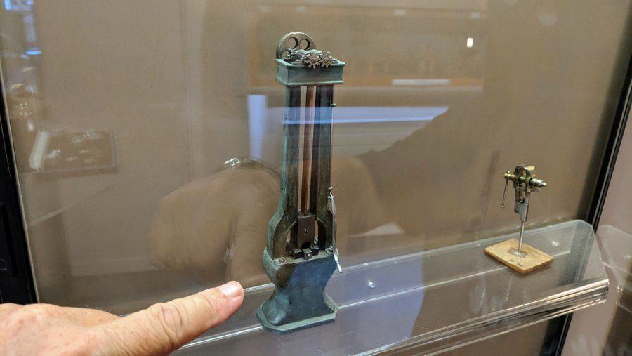 A very small model of a metal press in a reflective glass case