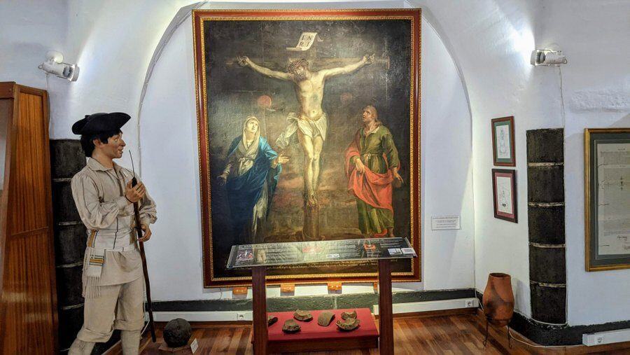 A pinting of Christ on the cross stand behind a display case with fragments of a large cannon ball