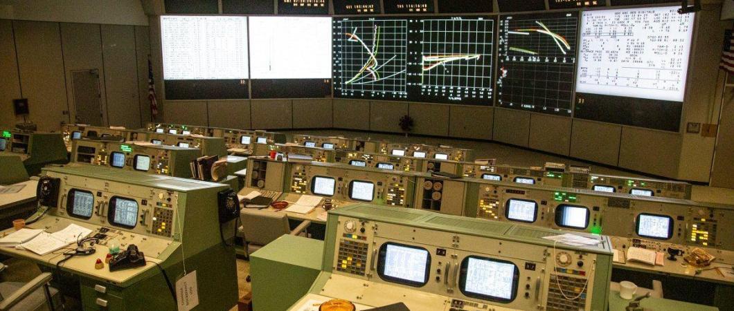 A view across the Mission Control Room with rows of consoles facing the wall screens