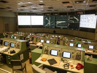 A view across the Mission Control Room with rows of consoles facing the wall screens