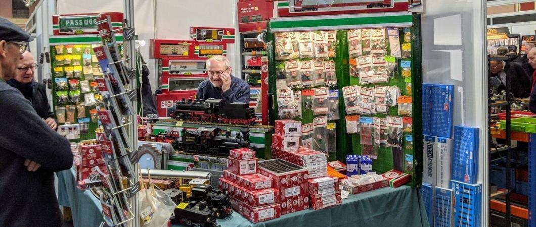 A stall holder at a model engineering exhibition is surrounded by model engines and accessories