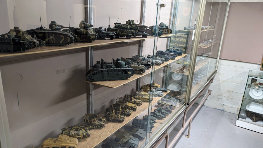 A glass display cabinet with shelves full of model tanks