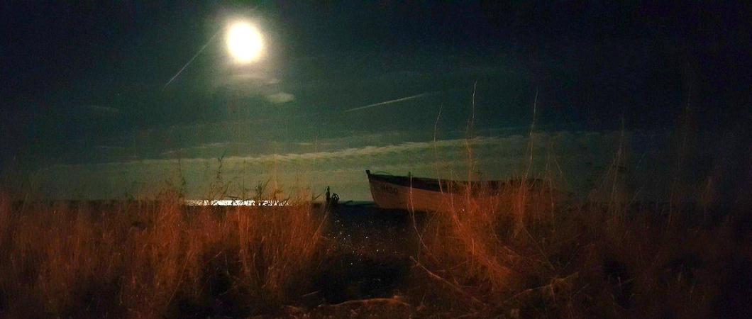 A bright moon illuminates a small fishing boat on a beach