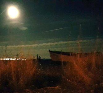 A bright moon illuminates a small fishing boat on a beach