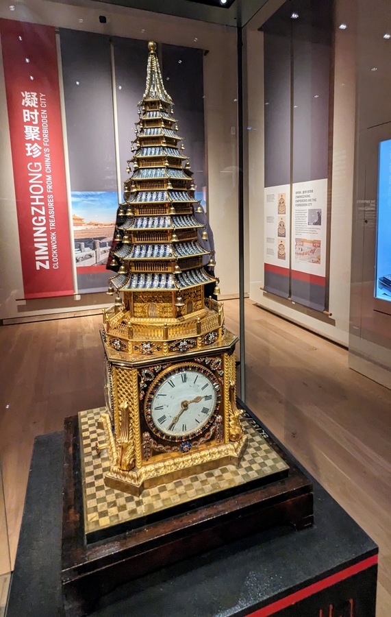 A tall blue and gold conical model of a pagoda with a clock in the base