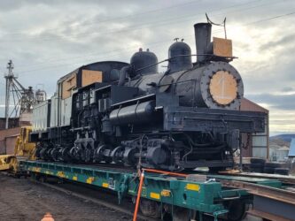 Black steam locomotive loaded onto a flat rail truck