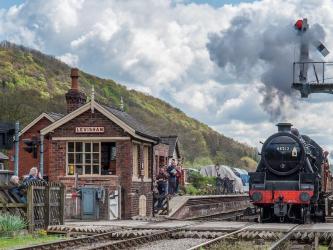 A steam train roars through a period railway station