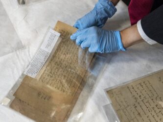 A man wearing protective rubber gloves, pulls old documents from a plastic folder