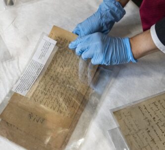 A man wearing protective rubber gloves, pulls old documents from a plastic folder