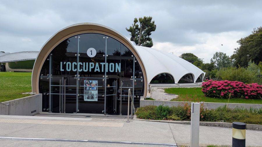 Glass entrance to a white building shaped like a parachute canopy.