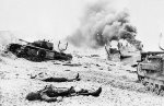 B/W photo of bodies of Canadian soldiers lying among damaged landing craft and 'Churchill' tanks of the Calgary Regiment following Operation 'Jubilee'