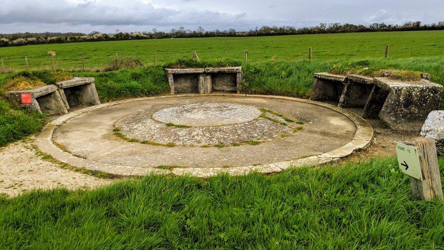 Circular concrete gun emplacement with concrete ammunition stores set around it into the earth defence wall