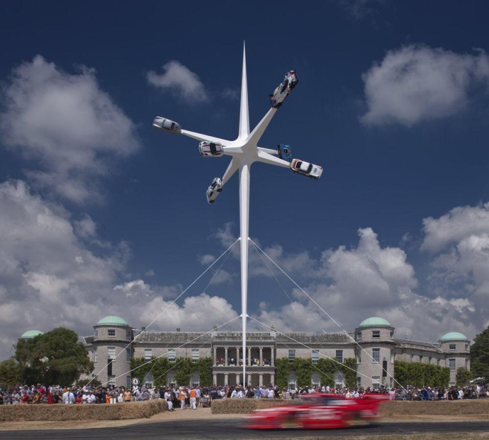 Six Porsche cars on spikes towering over Goodwood House on a sunny day