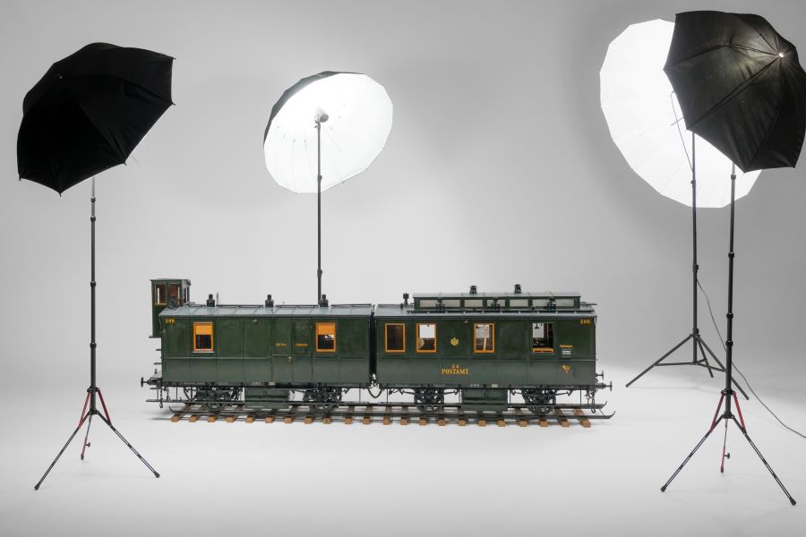 A large scale model of an Austrian 20th century post rail carriage, is illuminated under photographic spotlights