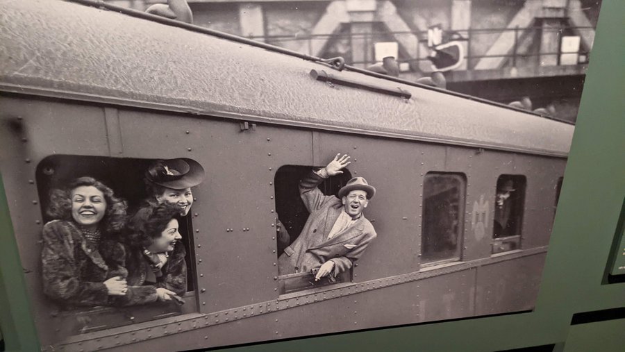Black & white photo of actors hanging out of a train window and waving as it departs