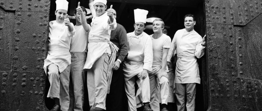 B/W photo of white uniformed chefs and kitchen staff at an open port of a ship