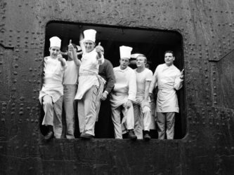 B/W photo of white uniformed chefs and kitchen staff at an open port of a ship