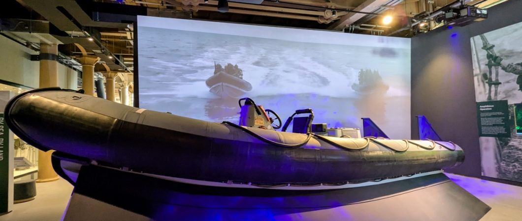 A large black Rigid Inflatable Boat in front of a large screen video showing a RIB in action
