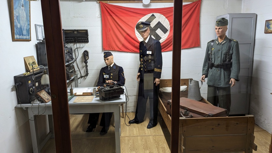 A German officer and his men in a radio room with a large red swastika flag on the wall