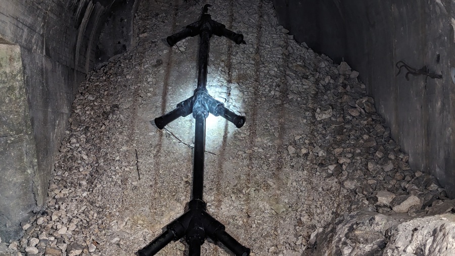 A close up of the black pipe laid up the rubble in one of the sloped gun shafts. It is shaped like the skeleton of a fish (herring bone) with pairs of short stubby pipes coming off the main pipe at regular intervals. It actually looks like a long length of black PVC toilet drainage pipe!