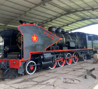 Black steam locomotive with red trim sits in a shed