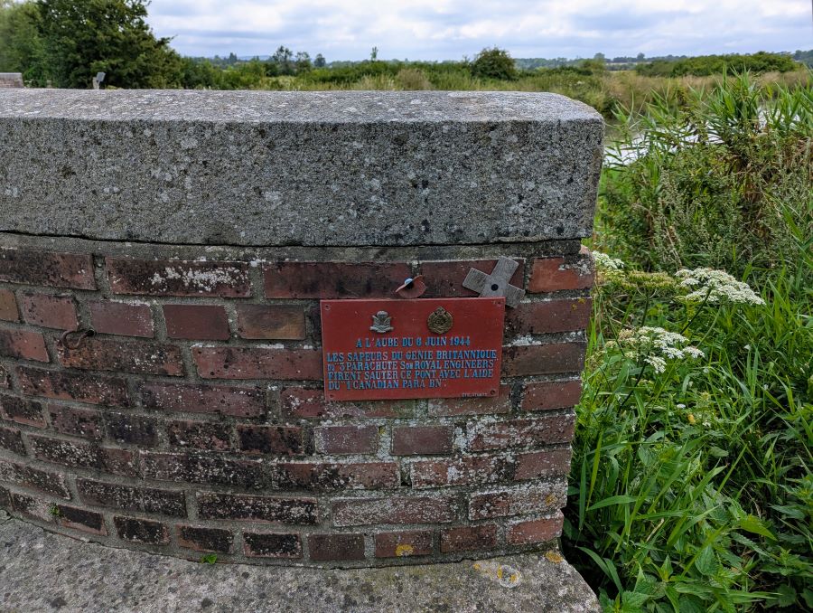 A small red plaque on the bridge brickwork acknowledges the roles of the Royal Engineers and Canadian paratroopers who blew up the previous bridge at this location on D-Day