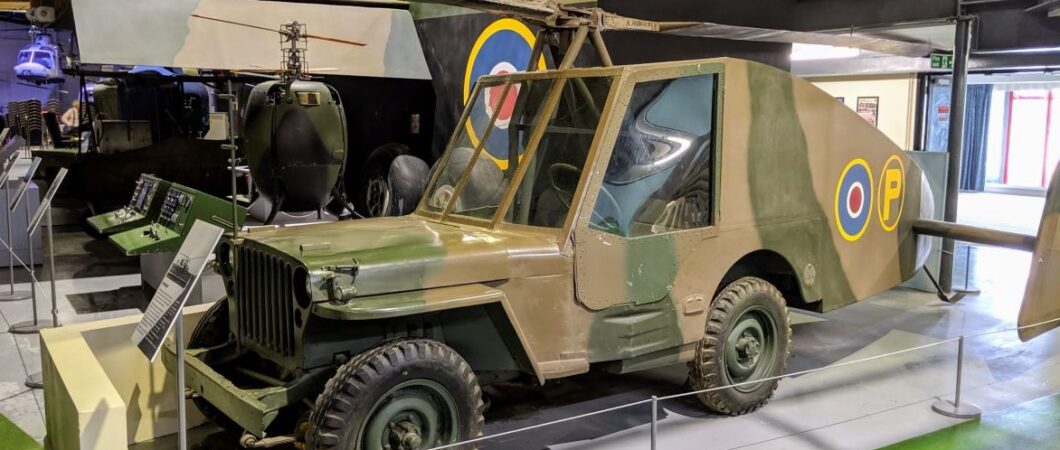 A grey and brown camouflaged Jeep with rotor blades and a long streamlined tail fitted with twin rudders