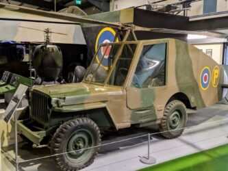 A grey and brown camouflaged Jeep with rotor blades and a long streamlined tail fitted with twin rudders