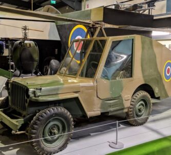 A grey and brown camouflaged Jeep with rotor blades and a long streamlined tail fitted with twin rudders