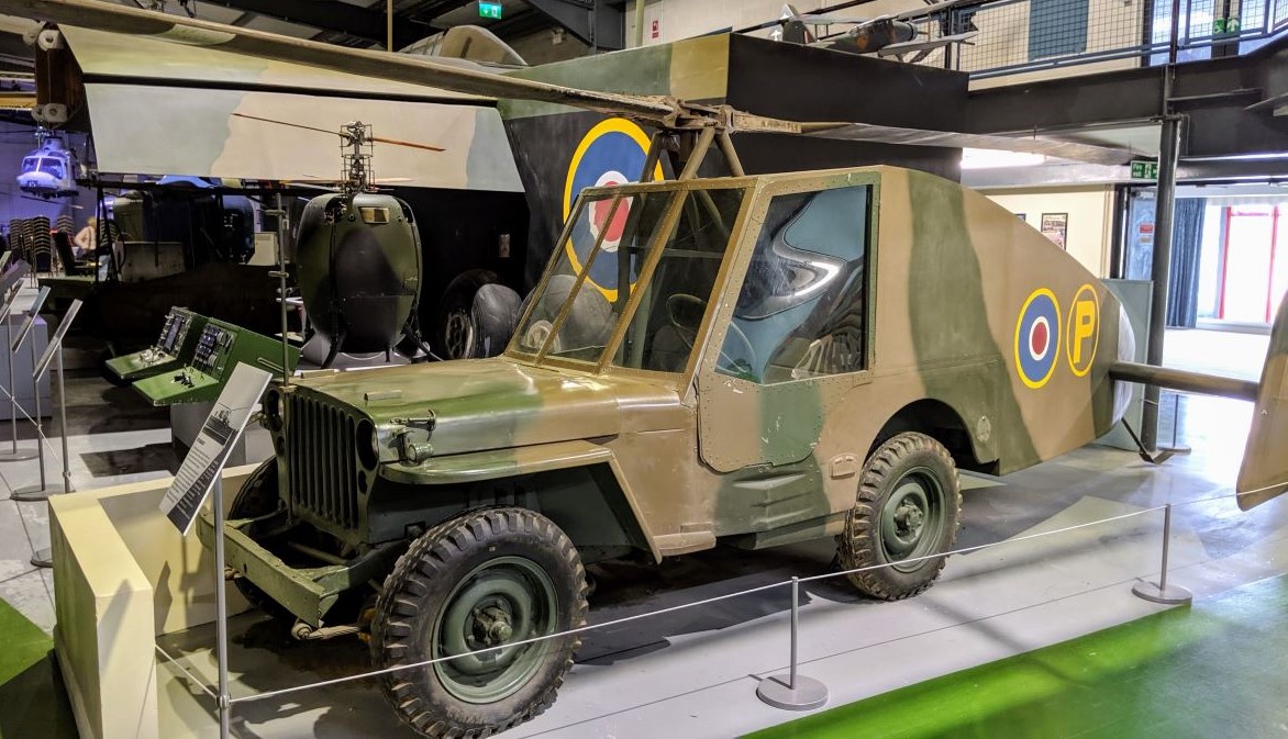 A grey and brown camouflaged Jeep with rotor blades and a long streamlined tail fitted with twin rudders