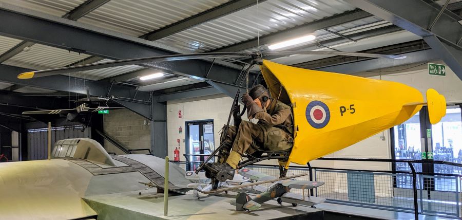 Small personal autogyro flown by a soldier in camouflaged uniform, and with a bright yellow streamlined tail section