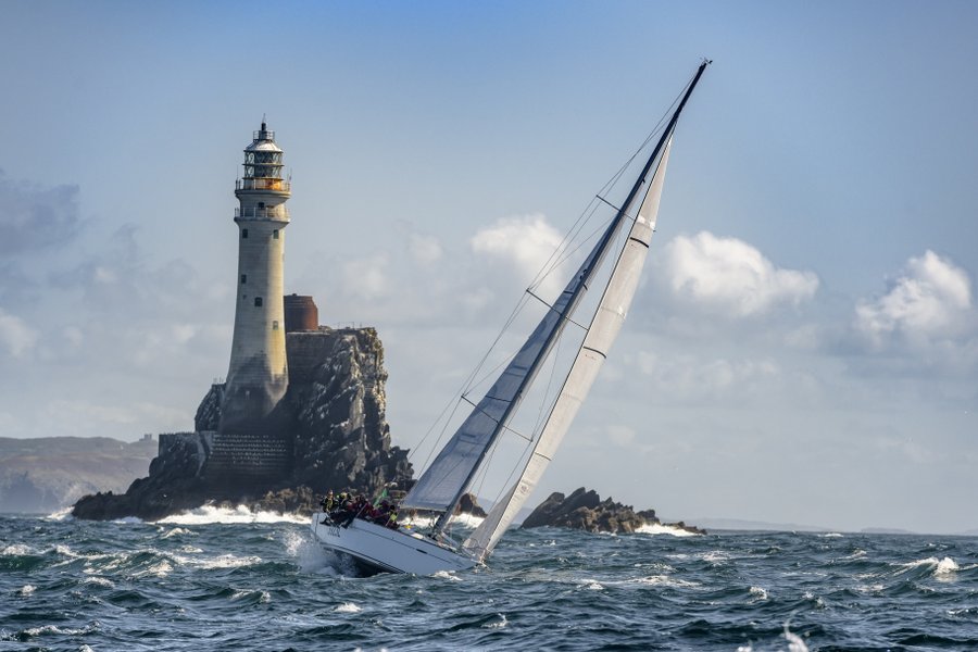 A yacht in the Rolex Fastnet race sails away from the dramatic Fastnet rock with its lighthouse