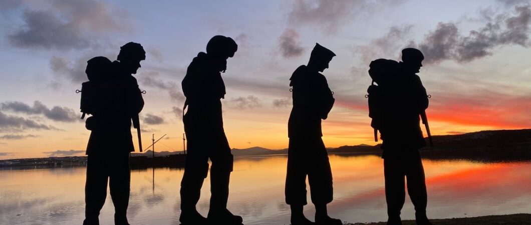 Four silhouettes of Falklands army, navy and air force personnel standing against a rich sunset