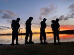 Four silhouettes of Falklands army, navy and air force personnel standing against a rich sunset
