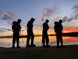 Four silhouettes of Falklands army, navy and air force personnel standing against a rich sunset