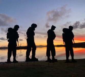 Four silhouettes of Falklands army, navy and air force personnel standing against a rich sunset