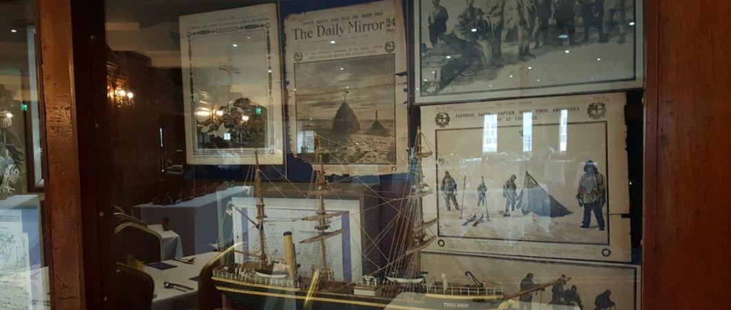 A glass display case with newspapers and ma ship model from 1910