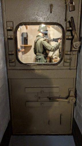 A German soldier behind a glass panelled door wearing a gas mask and firing through a slit