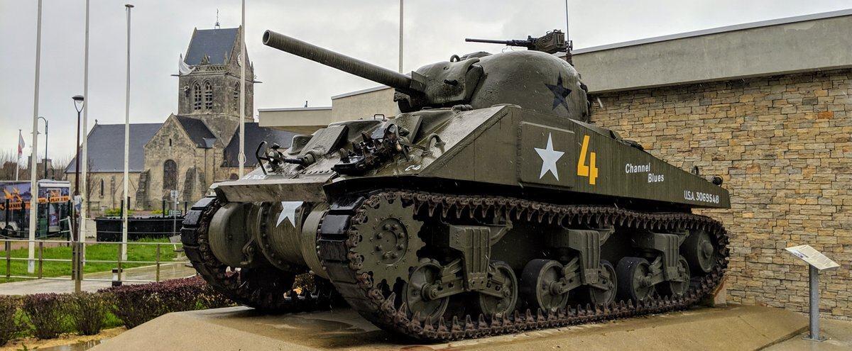A green tank with the church at Sainte-Mère-Église in the background