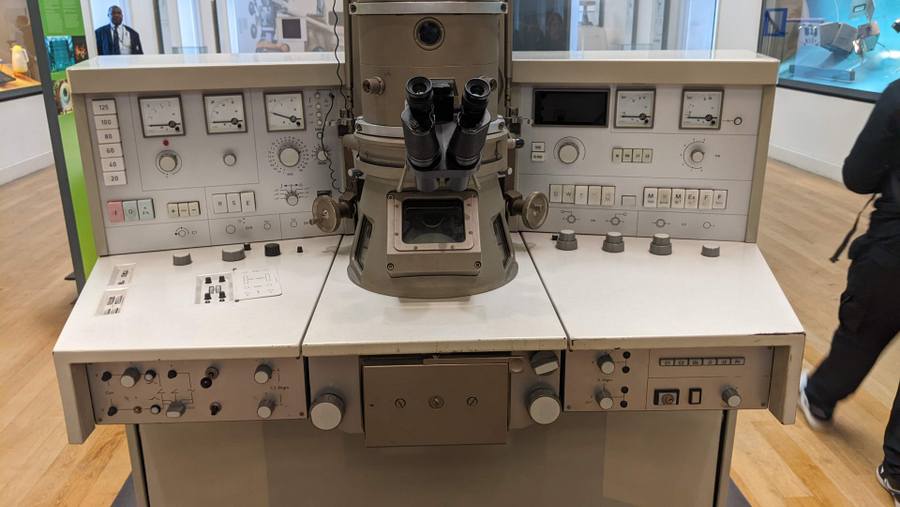 A desk unit with meters, dials, knobs and switches. In the centre of it is a large tube with eyepieces rather like a periscope.
