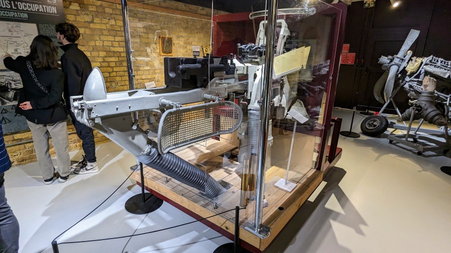 Grey painted gun and loading mechanism displayed in a glass case