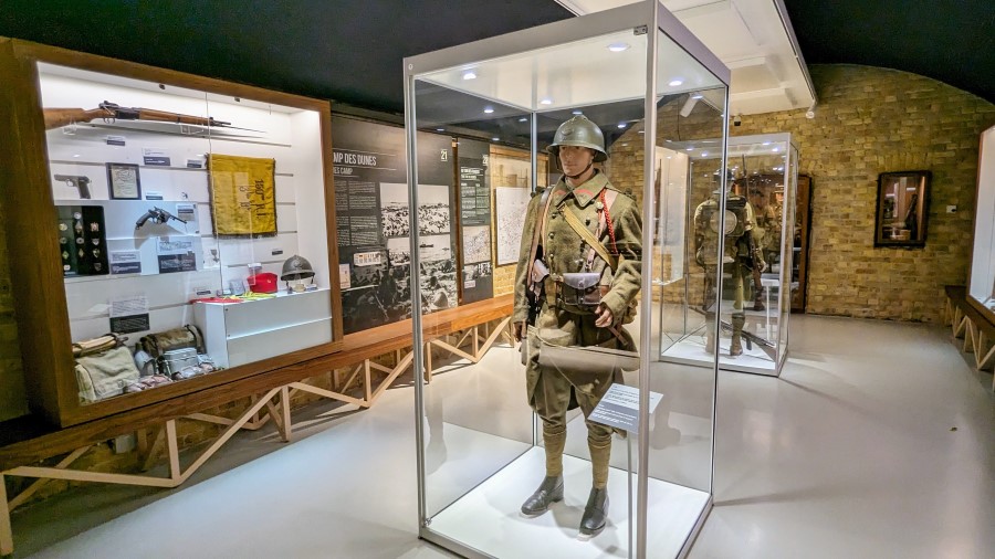 Uniformed soldiers (mannequins) in glass display boxes in a gallery at the Dynamo Museum, Dunkirk. There are info panels and other displays on the wall behind them