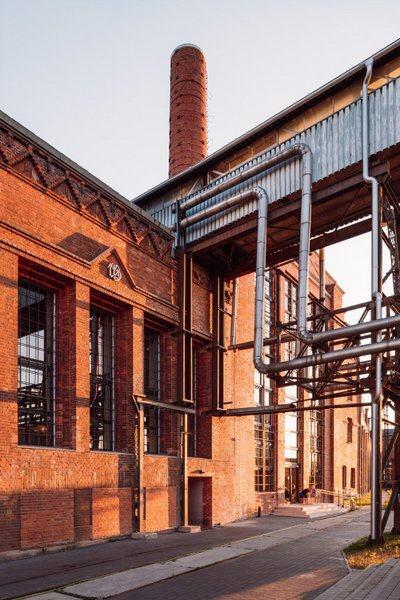 Stainless steel pipes and an aerial walkway lead to an ornate brick building at the Sugar Factory, all bathed in evening sunlight
