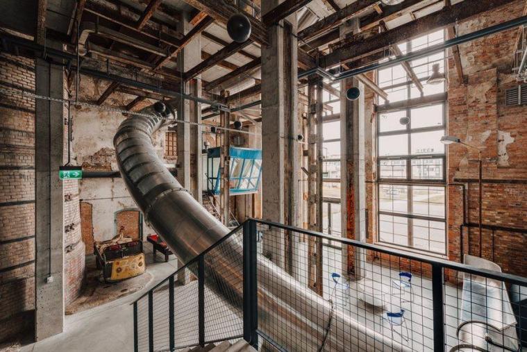 A huge stainless steel pipe curves its way above a lounge space with high floor-to-ceiling windows at the Sugar Factory