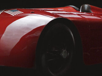 A streamlined classic racing car in glistening red paint. Sunbeam is painted in white letters on the front