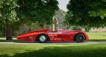 A sleek 100 year old racing car, the Sunbeam 1000hp, in shiny red paint is parked under some trees at the National Motor Museum, Beaulieu